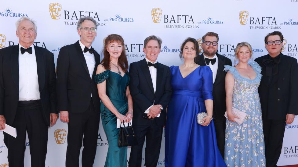 The cast of Gavin and Stacey at the BAFTAs- Robert Wilfort, Melanie Walters, Rob Brydon, Ruth Jones, James Corden, Joanna Page and Mathew Horne Brydon wears a black suit, whit shirt and black bow tie.