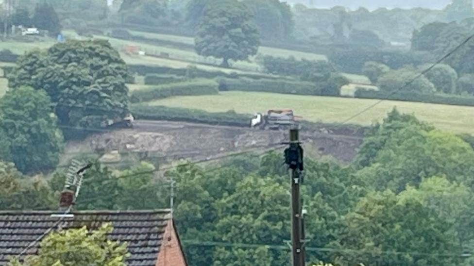 A lorry seen in the distance on a field behind houses