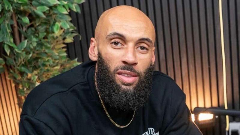 Aaron Dale, who is bald with a black beard and wearing a black sweatshirt and gold chain looks at the camera.