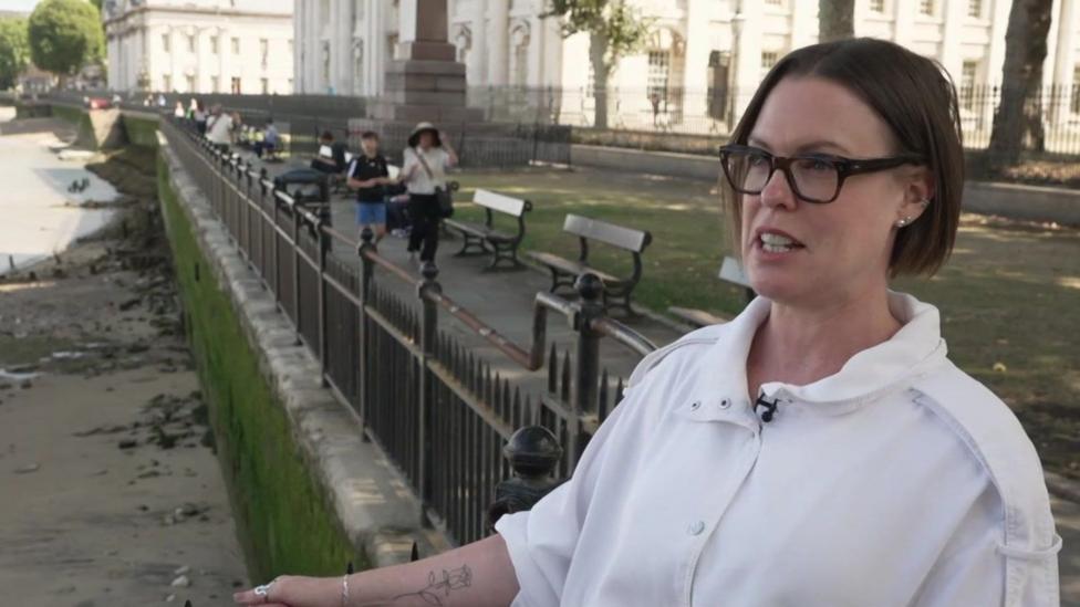 Emma Kelly, a woman with dark hair in a short bob, wearing a white shirt and glasses with a dark-coloured frame