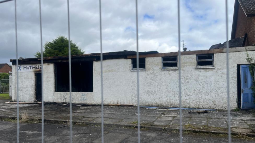 The derelict building which was set on fire. The picture is taken through silver metal bars.
