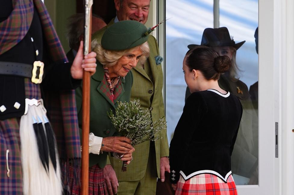 Queen Camilla accepts a bouquet from a young Highland dancer
