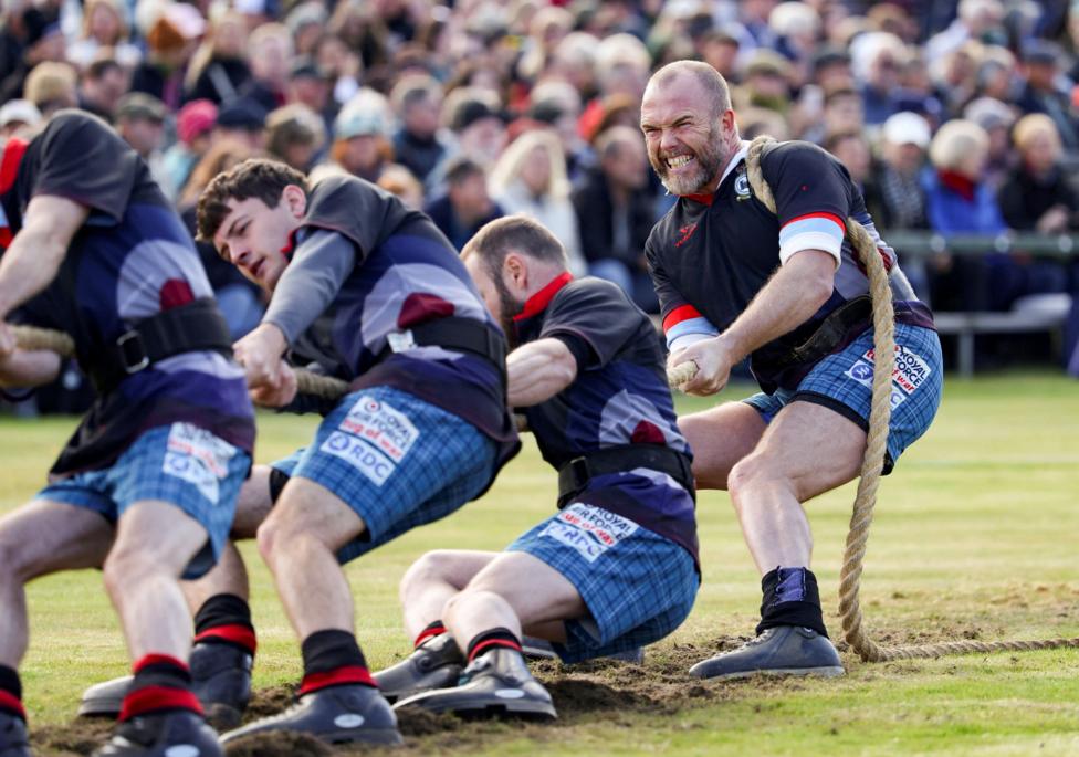men in black tops and blue shorts pull a rope in a tug of war match