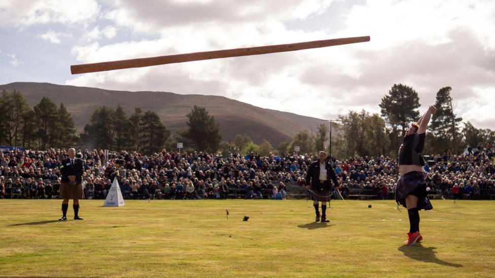 a man in a kilt and t-shit tossing a caber as spectators look on