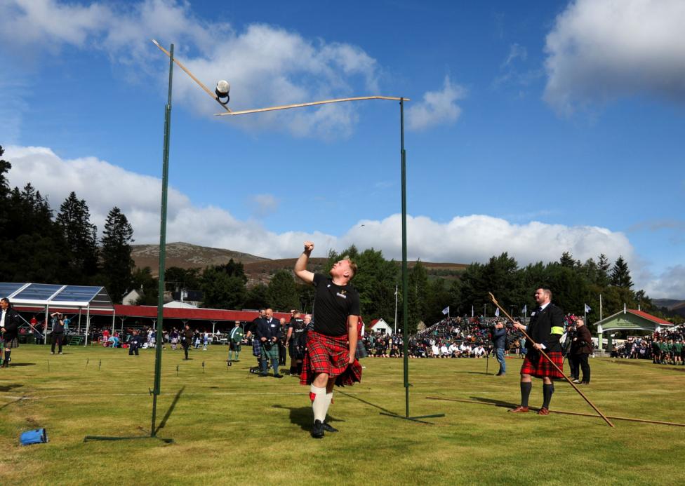 a kilted man looks up as a heavy weight he has thrown lands on and brakes a high bar