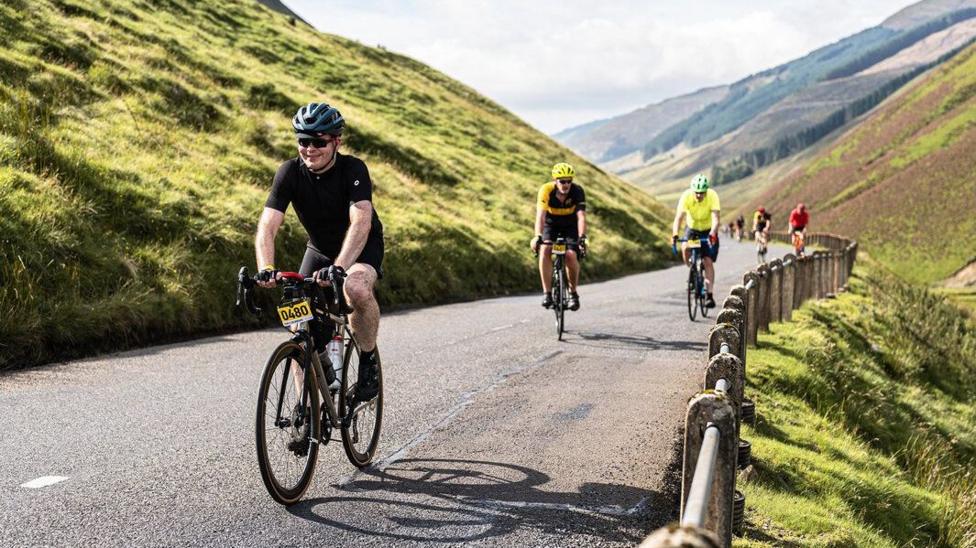Cyclists in lycra travelling along a road which cuts through a valley
