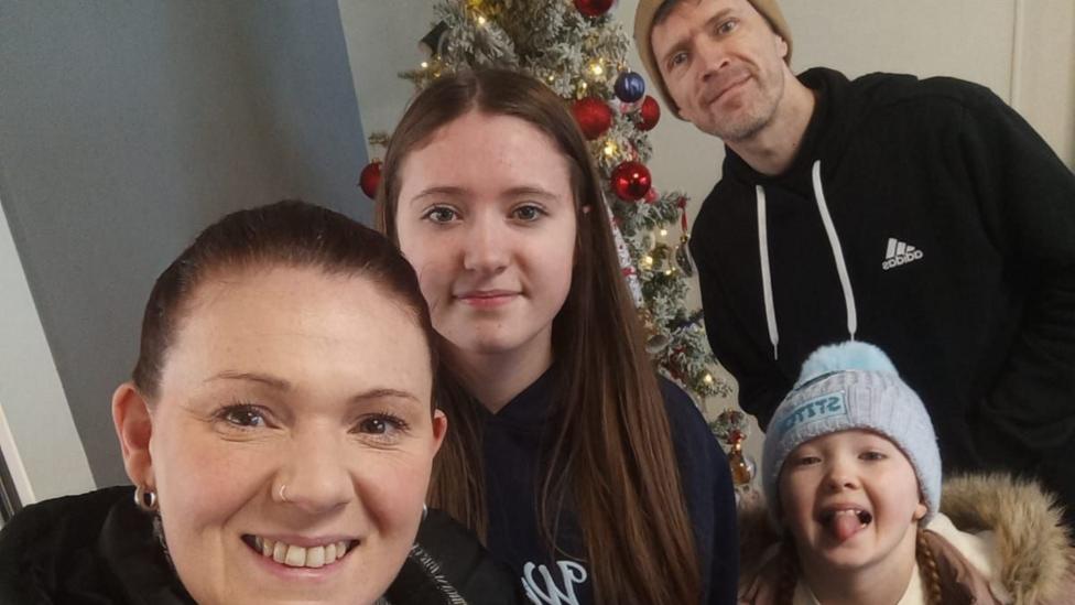Rhiannon, her partner and two daughters standing in front of a Christmas tree.