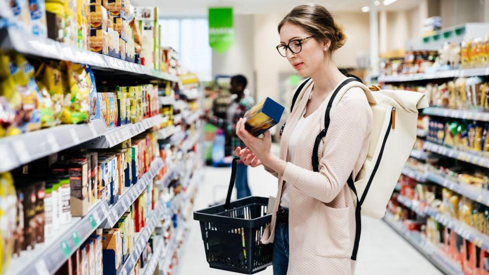 Woman looks at packet of biscuits in supermarket