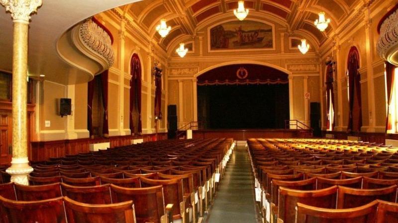 An interior photograph of the theatres at St Columb's Hall in Derry. Rows of red seats lead back from a stage