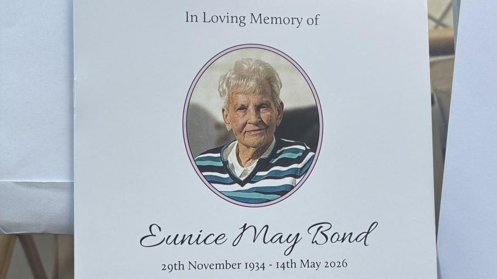 Eunice Bond's funeral booklet. It has a picture of her in an oval shape with white hair and a blue, green and white striped v-neck jumper on with a white shirt underneath.