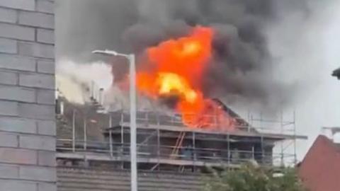 A building covered in scaffolding with flames emerging from the roof.