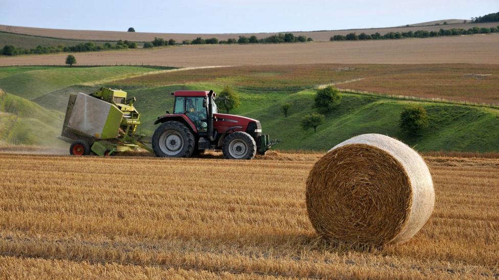 A tractor going through a field with a hay bale in front of it