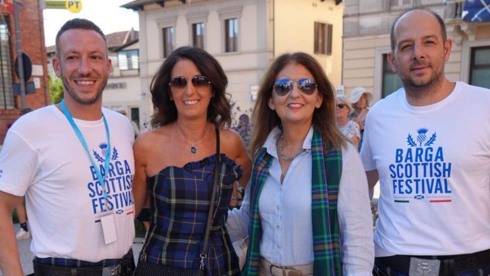 A group of people, two men in Barga Scottish Festival T-shirts and two women in sunglasses wearing tartan