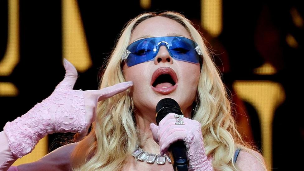 Madonna, wearing purple sunglasses and pink gloves, performing during a surprise concert in Times Square in New York City in June