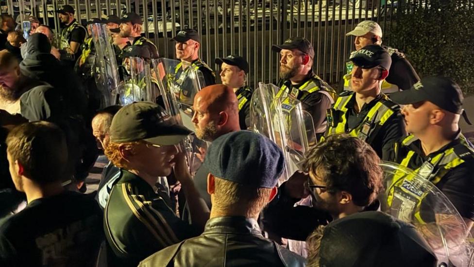 Protesters face off against riot police in Portsmouth. The officers, to the right of the image, are wearing hi-viz and carrying shields.