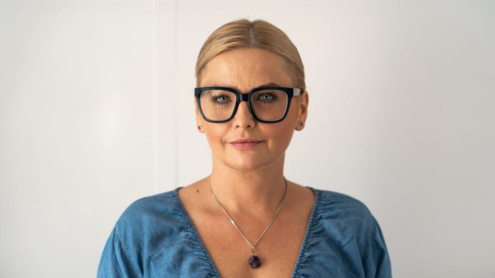 Kamilla Miller wears large black rimmed glasses and a blue blouse.