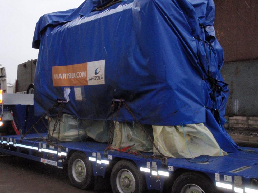 A large engine covered by a tarpaulin on the back of a low loaders