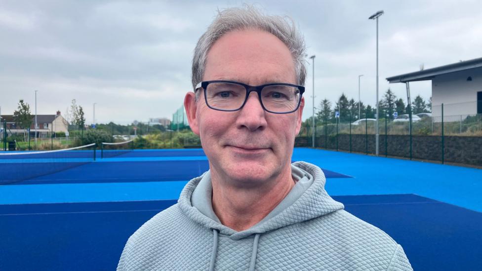 A man with grey hair and jumper, he has glasses