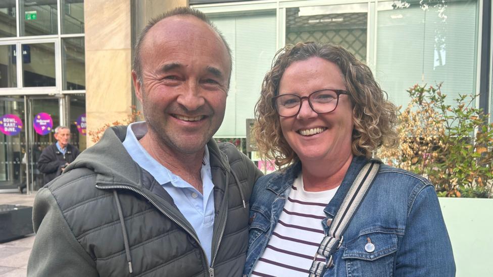 A man and a woman stand together smiling at the camera.