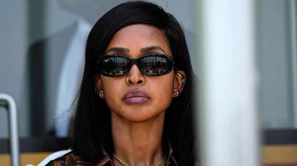 A close-up of Princess Ruth Komuntale with straight black hair, wearing dark sunglasses and several pieces of jewellery, including earrings, a nose ring and a necklace.