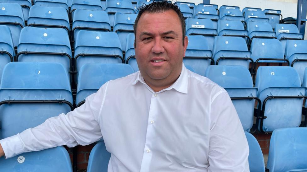 Gainsborough Trinity CEO Matt Boles pictured in a white shirt while sitting on blue seats at the club's home stadium