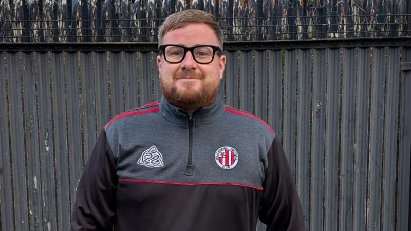 A man standing in a tracksuit wearing glasses.