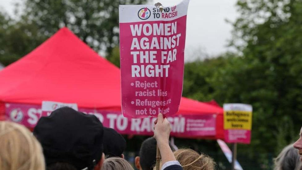 Protester holds a pink anti-racism sign which says 'Women Against the Far Right' above a crowd.