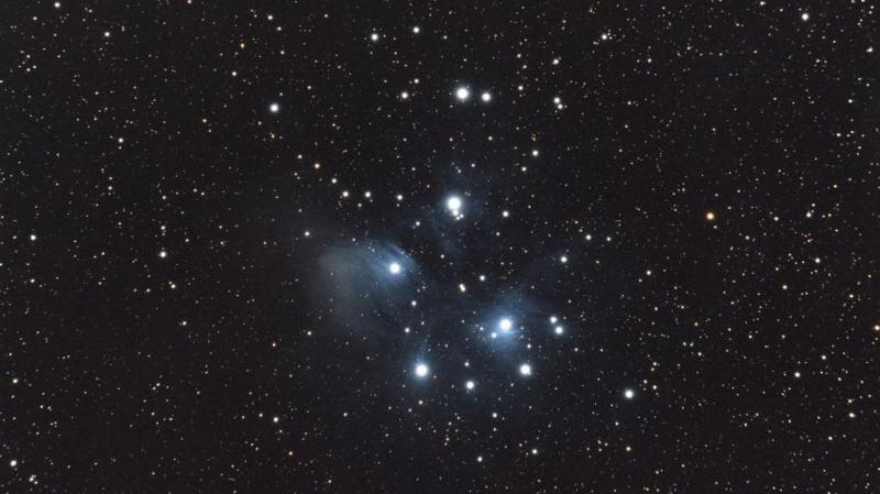 A group of stars shine bright white in the middle of starry black night sky.