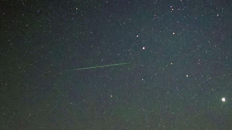 A green line cuts through a starry sky, capturing a meteor passing through the atmosphere.