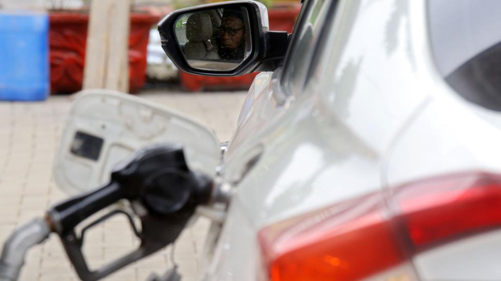 A white car is being refuelled at what appears to be a petrol station, with a fuel nozzle inserted into the vehicle's fuel tank.