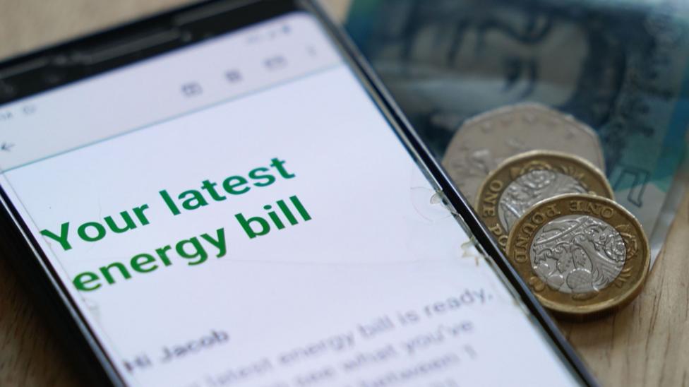A smartphone is lying on a wooden surface displaying what appears to be an email or online message headed “Your latest energy bill” in large green text.