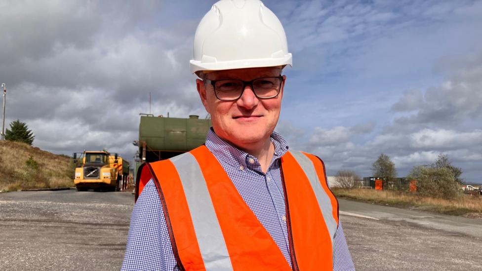 Simon Jones wears a hard hat and high vis jacket, as well as a pair of glasses.