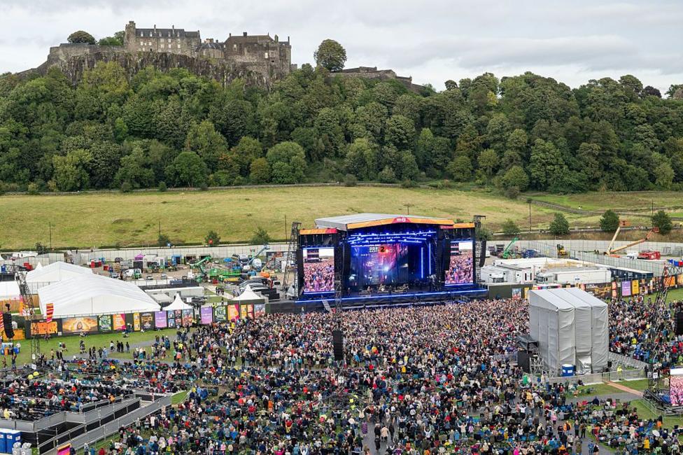 Festival taking place below Stirling Castle. There is a large stage with a large crowd of people and various tents and equipment