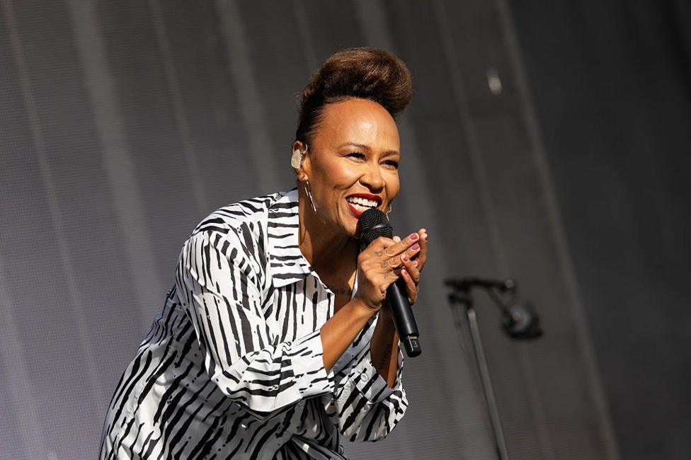 Emeli Sande is on stage leaning forward and singing into a microphone. She is wearing a black and white striped animal print shirt.