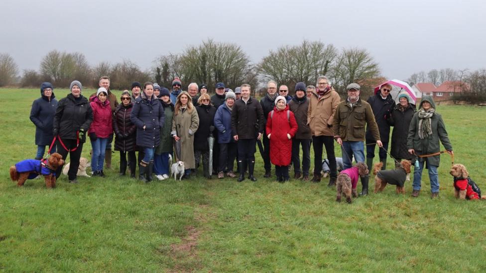 A group of people stood on a grassland on a cold rainy day