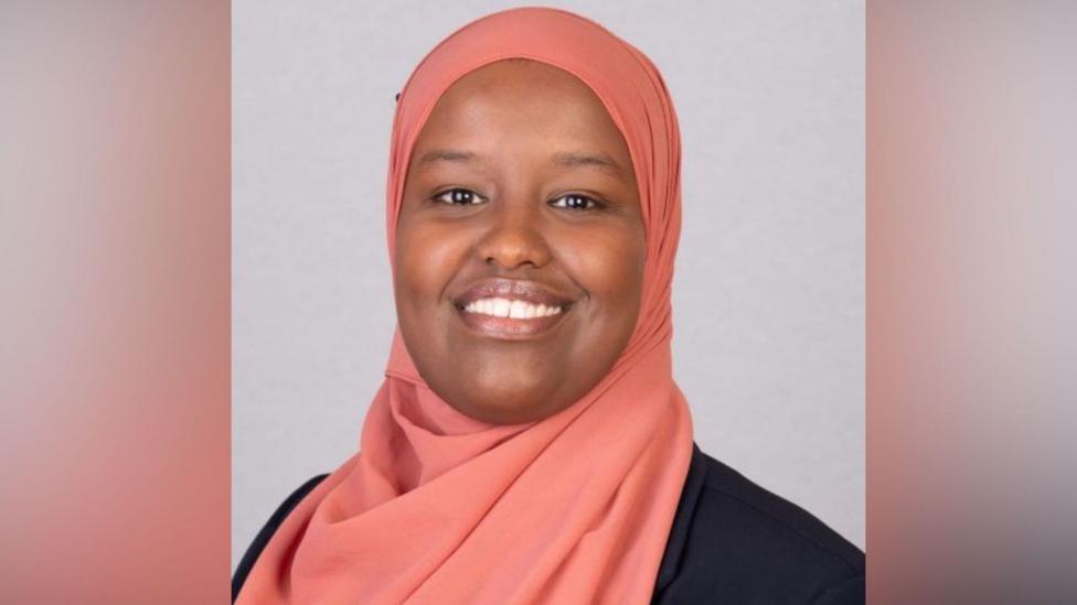 Sagal Abdi-Wali a young woman posing for an official photo in a peach coloured headsarf against a neutral background.