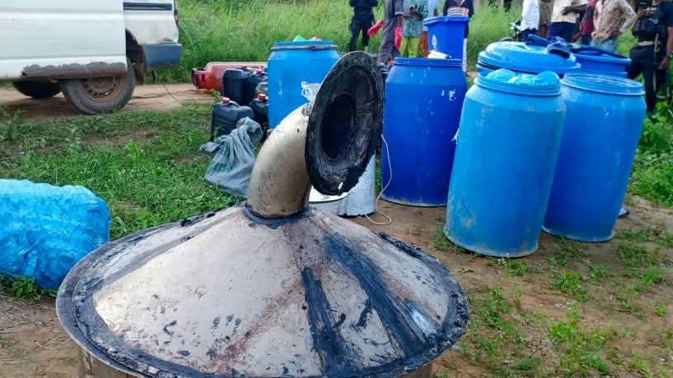 A funnel from a distillery is in the foreground and some blue barrels can be see in the background sitting on some patchy grass.