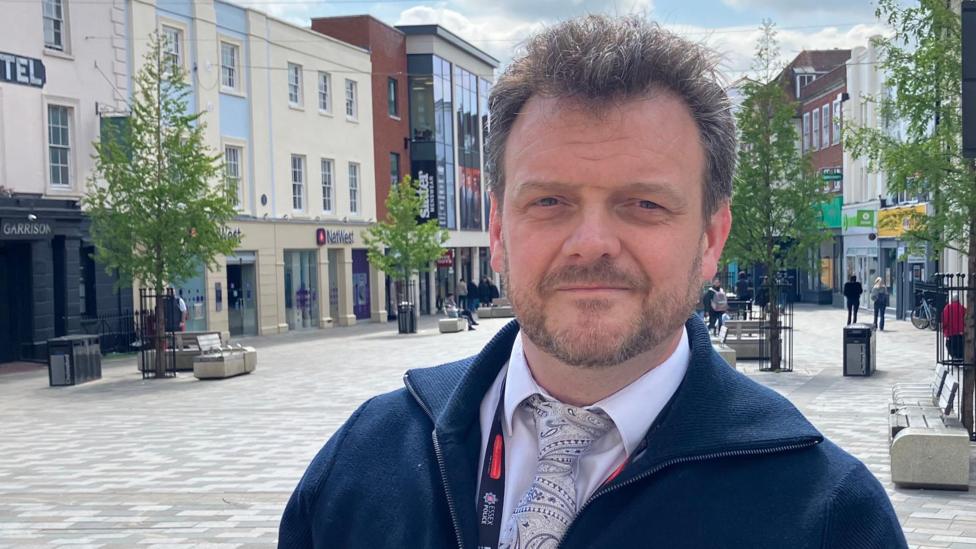 A head and shoulders picture of Sergeant Christian Denning from Essex Police in a pedestrianised area of Chelmsford city centre.
