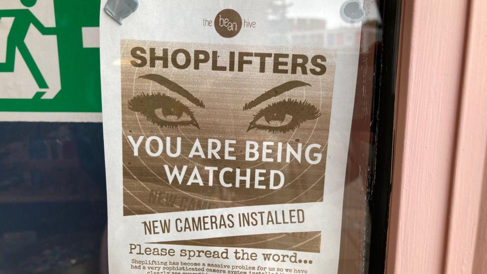 An A4 sign stuck to a wall in a shop. It warns shoplifters they are being watched via CCTV cameras.