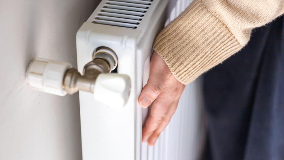 A hand at the end of a brown jumper touches a white radiator.