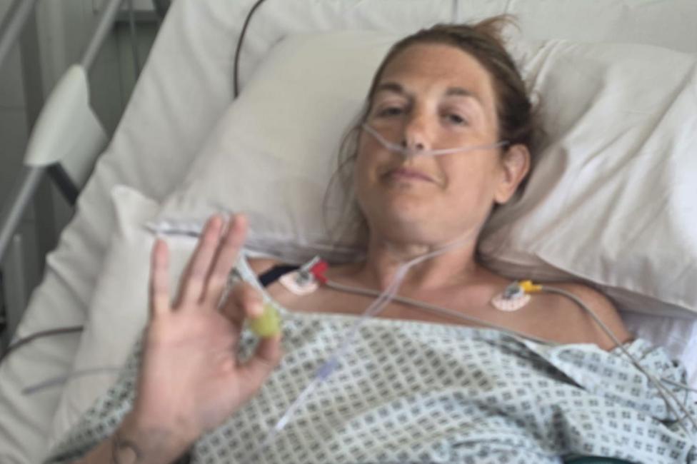 Karen is pictured in a hospital gown, lying in a hospital bed with tubes from her nose and other monitoring equipment