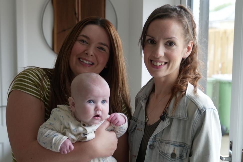 Lauren is smiling as she holds her six month old baby Grace who is looking up at the camera. She is standing next to fellow campaigner Kelly Dalley.