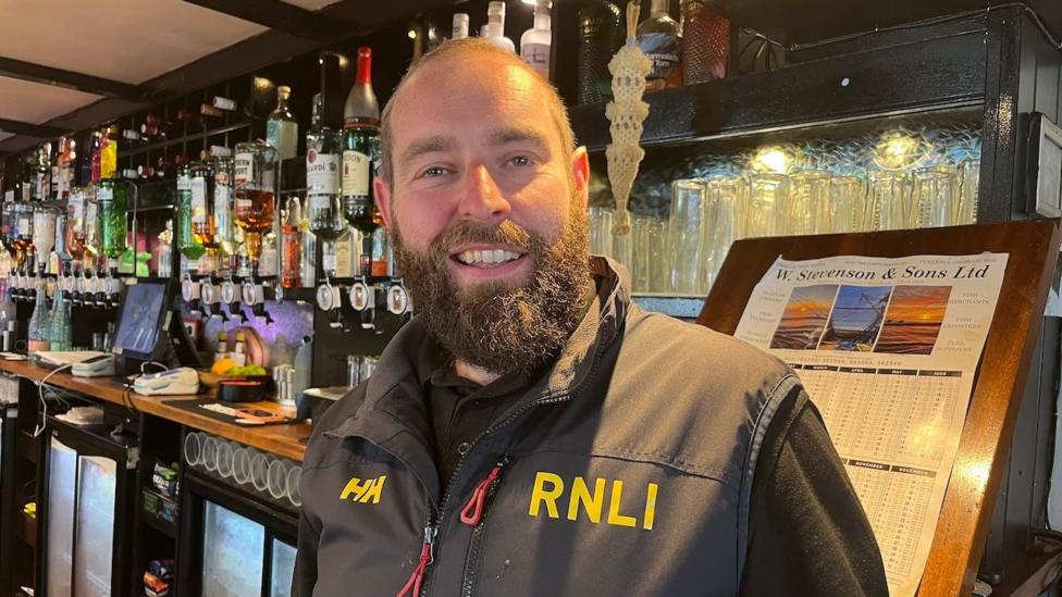 A man with a beard standing in front of a bar wearing an RNLI gillet