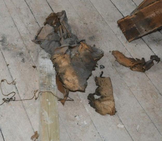 Remains of an old brown dusty newspaper, next to which is a thin brown twine, all lying on the floorboards