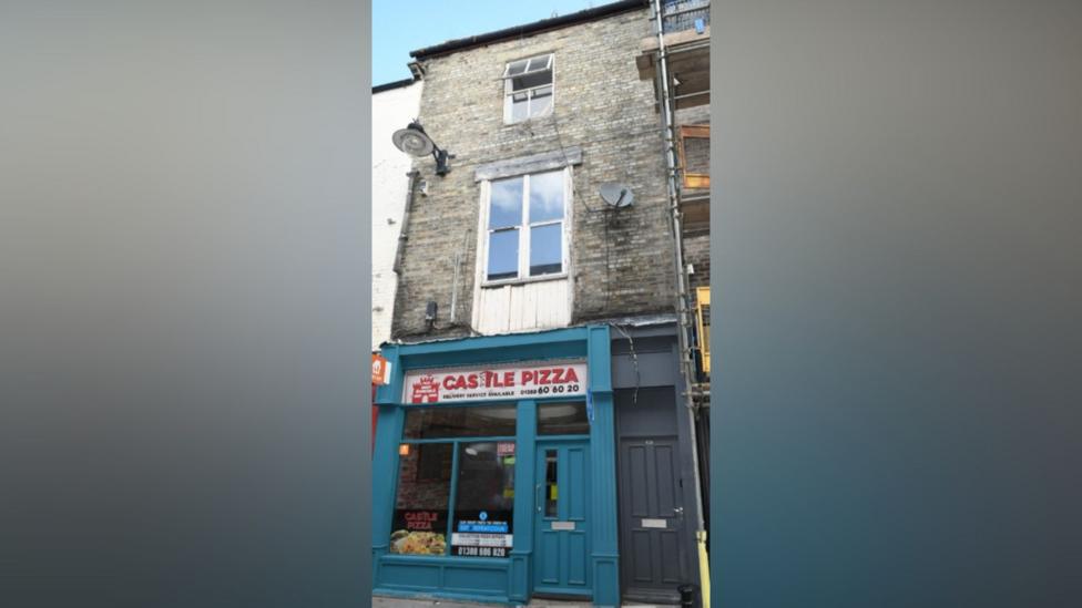 A three-storey terraced building where the baby was found. On the ground floor is a pizza shop called Castle Pizza, next to its green frontage is a black door and then two large windows above.