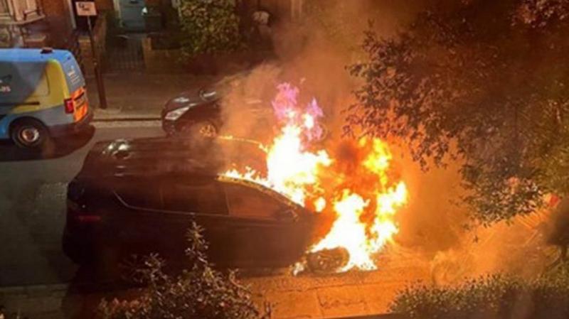 A burning car in a residential street at night
