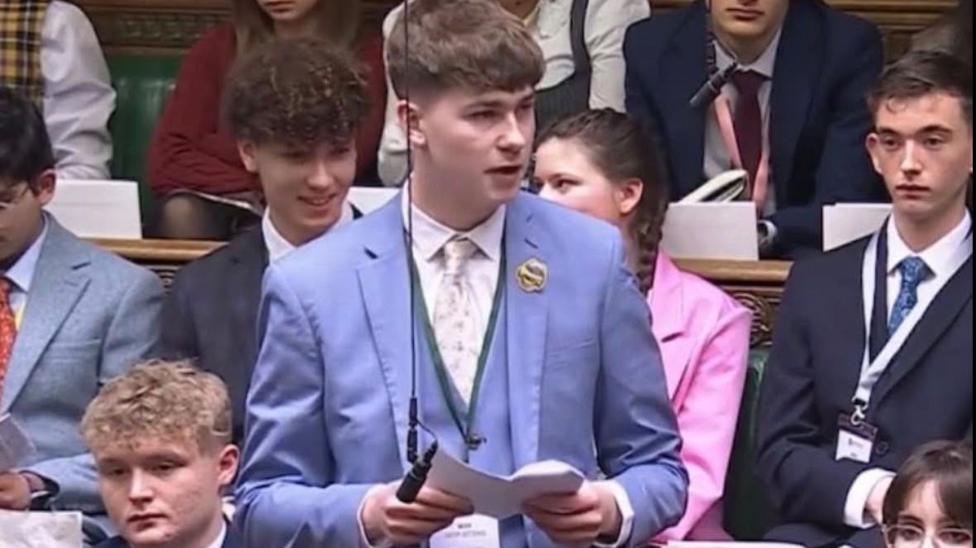 A young man in a light blue suit speaks in the House of Commons.