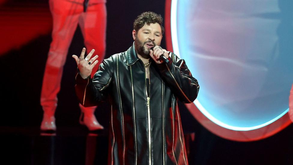 James Newman singing in a zipped up jacket on stage at the 2021 Eurovision grand final in Rotterdam