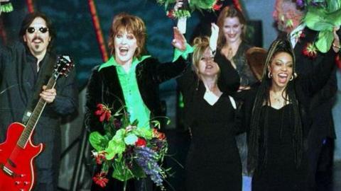 Katrina and the Waves waving towards the camera, celebrating their Eurovision win in 1997