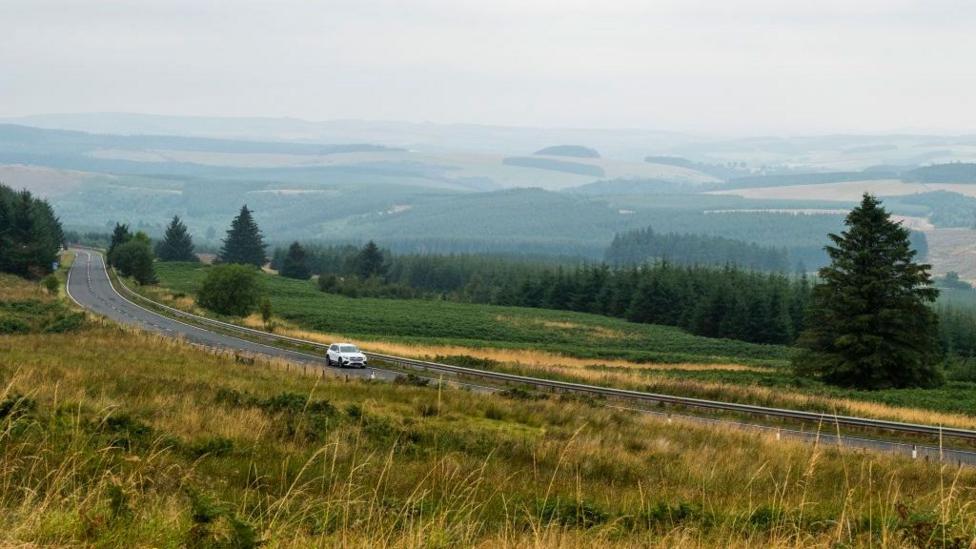 A winding road through the Borders with a white car on it